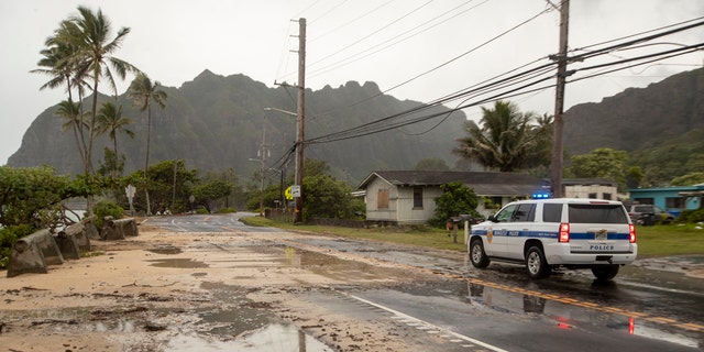 A police officer with the Honolulu Police Department inspects the sand and debris washed onto a closed portion of Kamehameha Highway, Sunday, July 26, 2020, in Kaaawa, Hawaii.