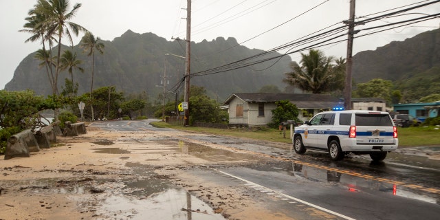 A police officer with the Honolulu Police Department inspects the sand and debris washed onto a closed portion of Kamehameha Highway, Sunday, July 26, 2020, in Kaaawa, Hawaii.