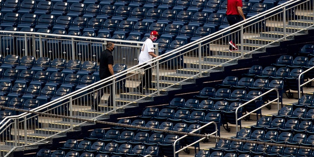 Director of the National Institute of Allergy and Infectious Diseases Dr. Anthony Fauci, center, walks through empty stands after throwing out the ceremonial first pitch at Nationals Park before the New York Yankees and the Washington Nationals play an opening day baseball game, Thursday, July 23, 2020, in Washington. (AP Photo/Andrew Harnik)