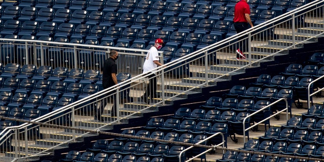 Director of the National Institute of Allergy and Infectious Diseases Dr. Anthony Fauci, center, walks through empty stands after throwing out the ceremonial first pitch at Nationals Park before the New York Yankees and the Washington Nationals play an opening day baseball game, Thursday, July 23, 2020, in Washington. (AP Photo/Andrew Harnik)