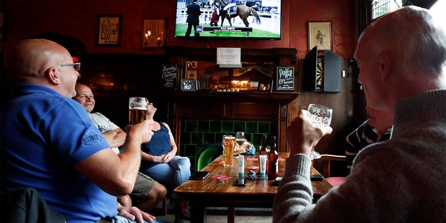 People enjoy their beers as they watch horse racing at the Forester pub in London, Saturday, July 4, 2020. England is embarking on perhaps its biggest lockdown easing yet as pubs and restaurants have the right to reopen for the first time in more than three months. In addition to the reopening of much of the hospitality sector, couples can tie the knot once again, while many of those who have had enough of their lockdown hair can finally get a trim. (AP Photo/Frank Augstein)