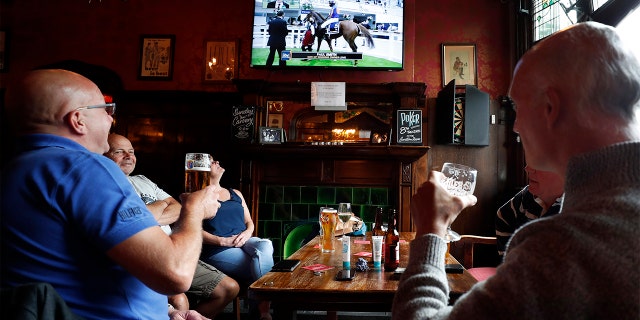 People enjoy their beers as they watch horse racing at the Forester pub in London, Saturday, July 4, 2020. England is embarking on perhaps its biggest lockdown easing yet as pubs and restaurants have the right to reopen for the first time in more than three months. In addition to the reopening of much of the hospitality sector, couples can tie the knot once again, while many of those who have had enough of their lockdown hair can finally get a trim. (AP Photo/Frank Augstein)