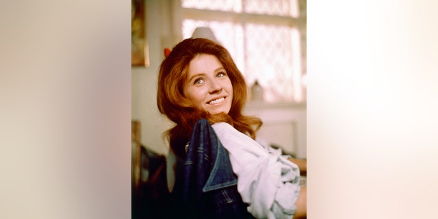 Patty Duke, US actress, smiling as she turns her head toward the camera for a portrait, while sitting in a chair with a denim jacket on the backrest, circa 1970.