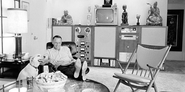 American entertainer Frank Sinatra (1915 - 1998) reads in his living room as his dog, Ringo, sits beside him, Palm Springs, California, 1965.