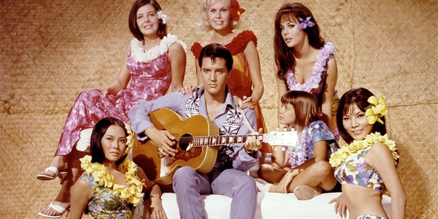 American singer and actor Elvis Presley surrounded by Linda Wong, Julie Parrish, Suzanna Leigh, Marianna Hill, Donna Butterworth (little girl), and Irene Tsu, on the set of 'Paradise, Hawaiian Style' directed by Canadian Michael D. Moore.