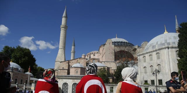 People, draped in Turkish flags, gather outside the Byzantine-era Hagia Sophia, one of Istanbul's main tourist attractions in the historic Sultanahmet district of Istanbul, following Turkey's Council of State's decision, Friday, July 10, 2020.