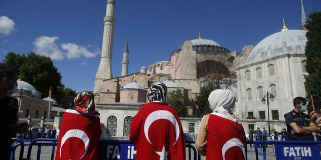 People, draped in Turkish flags, gather outside the Byzantine-era Hagia Sophia, one of Istanbul's main tourist attractions in the historic Sultanahmet district of Istanbul, following Turkey's Council of State's decision, Friday, July 10, 2020.
