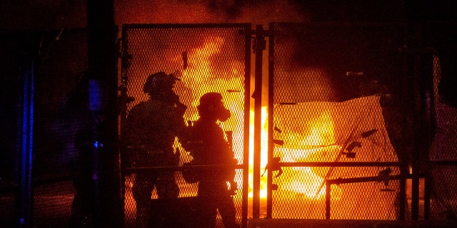Federal officers guard the Mark O. Hatfield U.S. Courthouse as a fire lit by protesters burns on the other side of a perimeter fence Saturday, July 25, 2020, in Portland, Ore. On the streets of Portland, a strange armed conflict unfolds night after night. It is raw, frightening and painful on both sides of an iron fence separating the protesters on the outside and federal agents guarding a courthouse inside. This weekend, journalists for The Associated Press spent the weekend both outside, with the protesters, and inside the courthouse, with the federal agents, documenting the fight that has become an unlikely centerpiece of the protest movement gripping America. (AP Photo/Noah Berger)