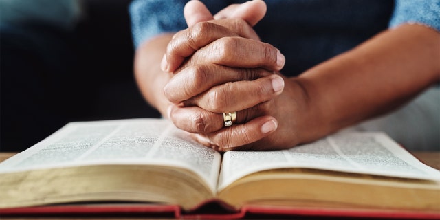 Closeup of an unrecognizable person's hands held over a bible at home during the day
