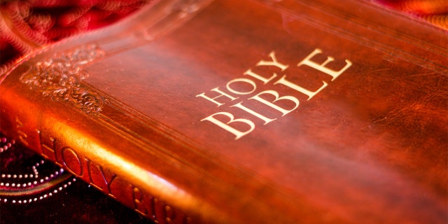 Holy Bible with pressed decorative leather cover on table with soft flickering candlelight
