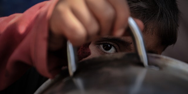 A Syrian boy looks through the handle of a cooking bowl as people queue up to receive food aid on October 7, 2019 in Idlib, Syria - file photo.
