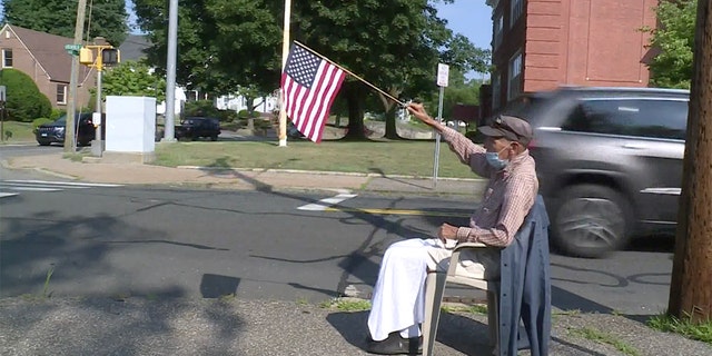 John Mastrocola, a 95-year-old World War II veteran, grabs his cane, a chair and an American flag every day at 8 a.m. and goes out to sit beside the sidewalk to wish his community a patriotic good morning. (Courtesy FOX61)