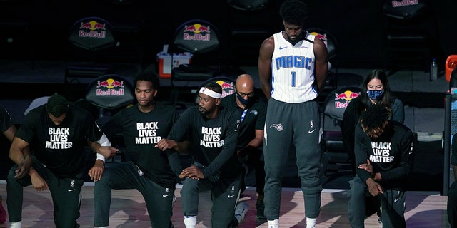 Orlando Magic's Jonathan Isaac stands as others kneel before the start of an NBA basketball game between the Brooklyn Nets and the Orlando Magic Friday, July 31, 2020, in Lake Buena Vista, Fla. (AP Photo/Ashley Landis, Pool)