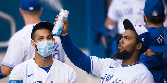Toronto Blue Jays left fielder Lourdes Gurriel Jr., left, watches teammate Teoscar Hernandez, right, spray sanitizer in the dugout during the first inning of an intersquad baseball action in Toronto on Friday, July 17, 2020. The Blue Jays have been denied approval by the Canadian government to play in Toronto amid the coronavirus pandemic.(Nathan Denette/The Canadian Press via AP)