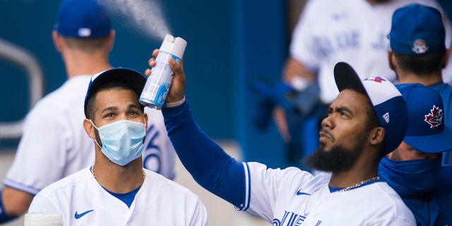 Toronto Blue Jays left fielder Lourdes Gurriel Jr., left, watches teammate Teoscar Hernandez, right, spray sanitizer in the dugout during the first inning of an intersquad baseball action in Toronto on Friday, July 17, 2020. The Blue Jays have been denied approval by the Canadian government to play in Toronto amid the coronavirus pandemic.(Nathan Denette/The Canadian Press via AP)