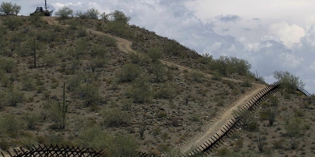 In this July 29, 2010, file photo, a U.S. National Guard vehicle guards covered under camouflage fabric sits atop a mountain next to the border fence near Sonoyta, Mexico. (AP Photo/Guillermo Arias)