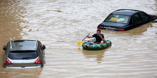 In this photo released by Xinhua News Agency, a man paddles with an inflatable boat past submerged cars during a flood in Rongshui County in southern China's Guangxi Zhuang Autonomous Region, July 11.