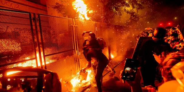 Protesters throw flaming debris over a fence at the Mark O. Hatfield United States Courthouse on Wednesday, July 22, 2020, in Portland, Ore. Following a larger Black Lives Matter Rally, several hundred demonstrators faced off against federal officers at the courthouse. (AP Photo/Noah Berger)