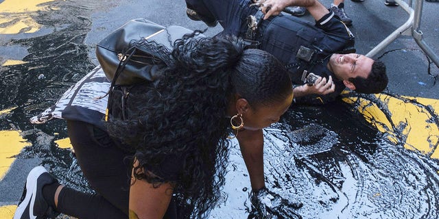 An NYPD officer slips and falls during an attempt to detain a protester pouring black paint on the Black Lives Matter mural outside of Trump Tower on Fifth Avenue in the Manhattan borough of New York on Saturday. (AP Photo/Yuki Iwamura)