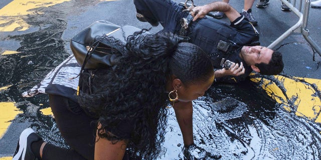 An NYPD officer slips and falls during an attempt to detain a protester pouring black paint on the Black Lives Matter mural outside of Trump Tower on Fifth Avenue in the Manhattan borough of New York on Saturday. (AP Photo/Yuki Iwamura)