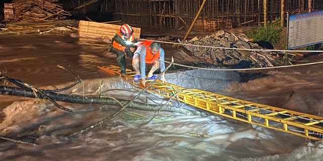 A rescuer helps a worker cross a ladder to get across floodwaters from a construction site in Jing'an county in central China's Jiangxi province midnight Friday, July 3, 2020.