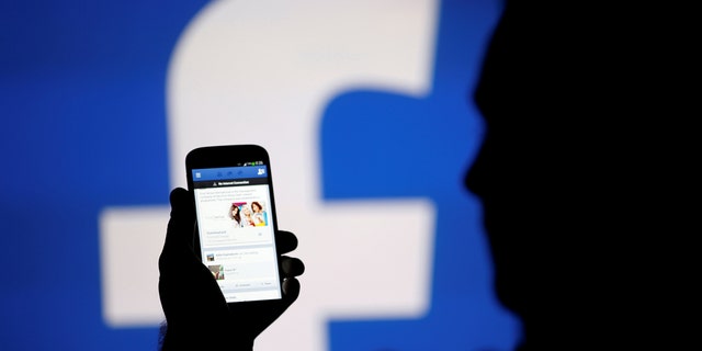 A man is silhouetted against a video screen with a Facebook logo. REUTERS/Dado Ruvic