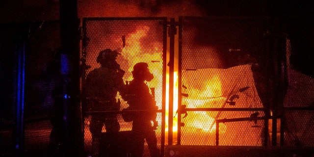 Federal officers guard the Mark O. Hatfield U.S. Courthouse as a fire lit by protesters burns on the other side of a perimeter fence Saturday, July 25, 2020, in Portland, Ore. (AP Photo/Noah Berger)