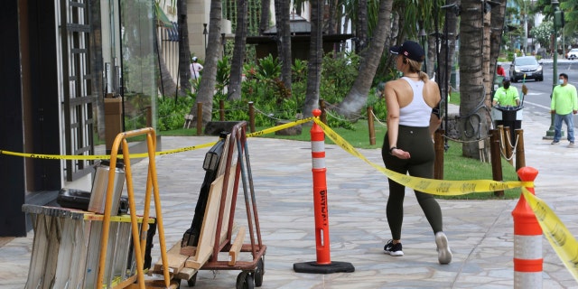 A woman walks past boarded storefronts in the Waikiki neighborhood of Honolulu, Saturday, July 25, 2020, as Hurricane Douglas approaches.