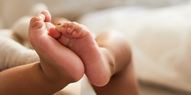 Close-up of an unrecognizable cute baby waving while lying in bed.  AAP is a sleeping product that meets the safety standards of the Consumer Product Safety Commission for cribs, bassinets, playpen and bedside sleepers, and recommends that your baby sleep on a flat, firm, non-sloping surface.  CNN. 