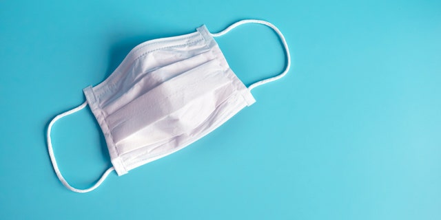 Close up white surgical face mask on a blue-green background.