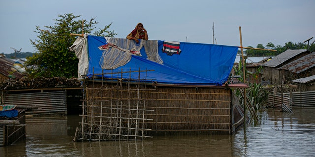 A flood affected Indian woman stands on the roof of her partially submerged house along river Brahmaputra in Morigaon district, Assam, India, July 16.
