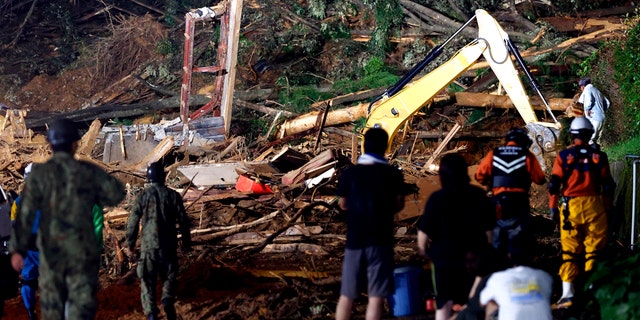 People watch a search operation at the site of a mudslide in Ashikita town, Kumamoto prefecture, southwestern Japan, Saturday, July 4, 2020.