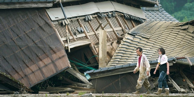 A couple walks in front of houses damaged by flood in Kuma village, Kumamoto prefecture, southwestern Japan, Sunday, July 5, 2020.