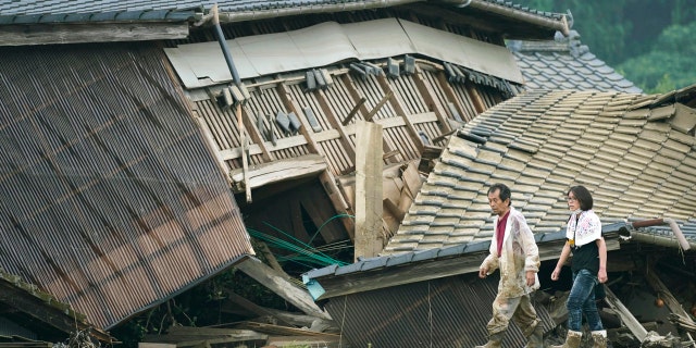 A couple walks in front of houses damaged by flood in Kuma village, Kumamoto prefecture, southwestern Japan, Sunday, July 5, 2020.