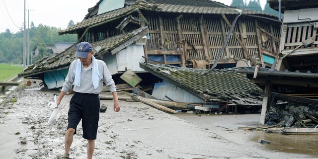 A man walks on muddy road past houses damaged by flood in Kuma village, Kumamoto prefecture, southwestern Japan, Sunday, July 5, 2020.