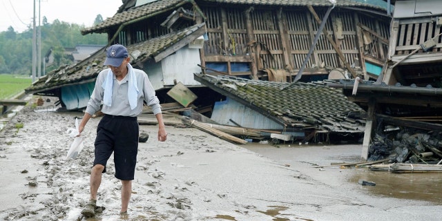 A man walks on muddy road past houses damaged by flood in Kuma village, Kumamoto prefecture, southwestern Japan, Sunday, July 5, 2020.