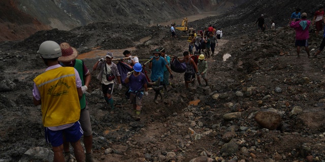 Rescue workers use poles to carry bodies shrouded in blue and red plastic sheets July 2, in Hpakant, Kachin State, Myanmar.