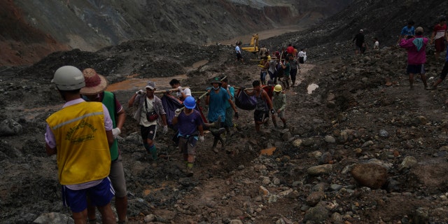 Rescue workers use poles to carry bodies shrouded in blue and red plastic sheets July 2, in Hpakant, Kachin State, Myanmar.