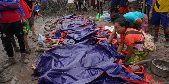 Women look at bodies shrouded in blue and red plastic sheets placed in a row on the ground July 2, in Hpakant, Kachin State, Myanmar.