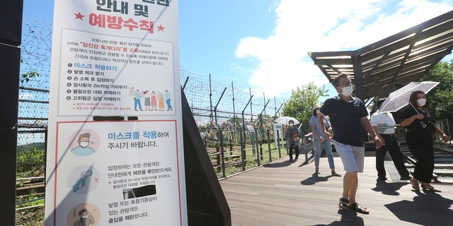 People wearing face masks to help protect against the spread of the new coronavirus pass by a notice about precautions against the coronavirus disease at the Imjingak Pavilion in Paju, near the border with North Korea, Sunday, July 26, 2020.