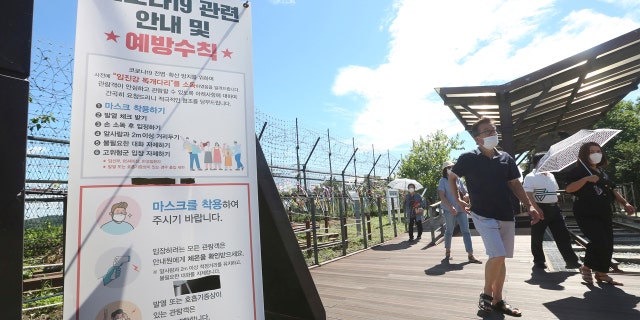 People wearing face masks to help protect against the spread of the new coronavirus pass by a notice about precautions against the coronavirus disease at the Imjingak Pavilion in Paju, near the border with North Korea, Sunday, July 26, 2020.