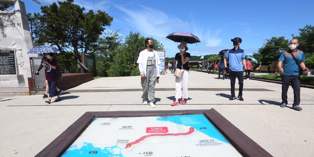 People wearing face masks to help protect against the spread of the new coronavirus walk by a map of two Koreas showing North Korea's capital Pyongyang and South Korea's capital Seoul at the Imjingak Pavilion in Paju, near the border with North Korea, Sunday, July 26, 2020.