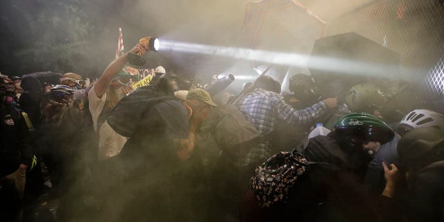 Demonstrators push on a fence as tear gas is deployed during a Black Lives Matter protest at the Mark O. Hatfield United States Courthouse on Saturday in Portland, Ore. (AP Photo/Marcio Jose Sanchez)