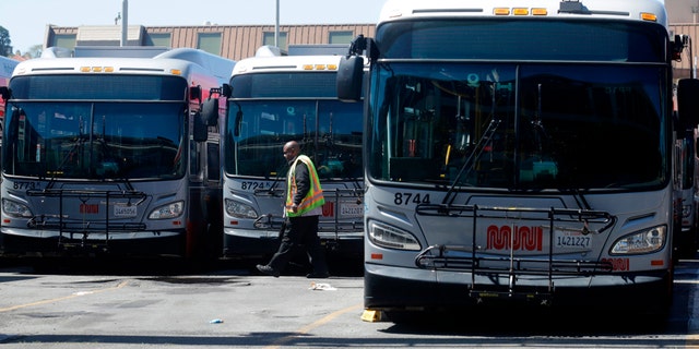 In this April 7, 2020, file photo, a Muni worker walks in front of buses at a San Francisco Municipal Transportation Agency yard in San Francisco. (AP Photo/Jeff Chiu, File)