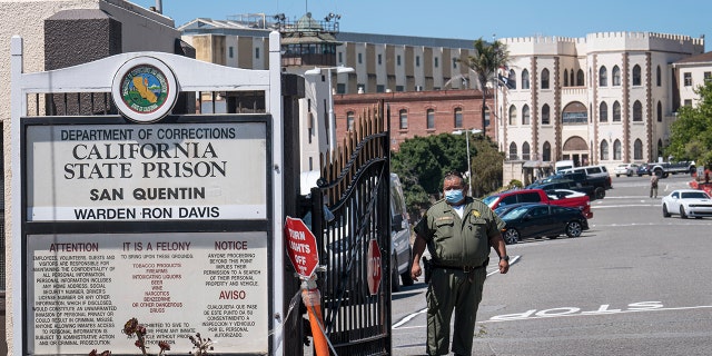 A California Department of Corrections and Rehabilitation (CDCR) officer wearing a protective mask stands at the front gate of San Quentin State Prison in San Quentin, California. Photographer: David Paul Morris/Bloomberg via Getty Images