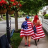 Parade-goers draped in American flags walk down the street before a Fourth of July parade in Bristol, Rhode Island, July 4, 2020.