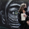 A woman wearing a face mask walks past a mural of an Indigenous man in Bogota, Colombia, July 3, 2020.