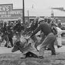 A state trooper swings a billy club at John Lewis, right foreground, chairman of the Student Nonviolent Coordinating Committee, to break up a civil rights voting march in Selma, AL, March 7, 1965.