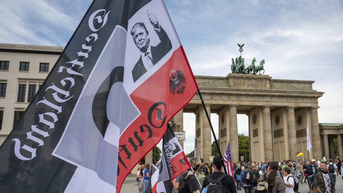 A protester holds a flag featuring a picture of President Trump in front of the Brandenburg Gate before a demonstration against the coronavirus measures by the German Government in Berlin, Germany, Saturday, Aug. 29, 2020. (Christophe Gateau/dpa via AP)