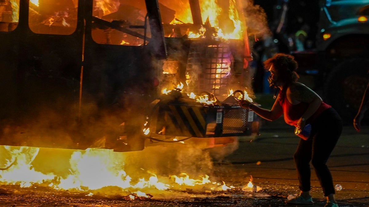 A protester lights a cigarette on a garbage truck that was set on fire during protests late Monday in Kenosha, Wis